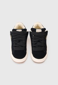 Sneakers in suede nera con spesse stringhe nere, interno beige e suole in gomma bianca. Presentano un accento dorato con il logo sul lato.