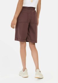 Bordeaux korte broek met een elastische tailleband, twee achterzakken en een omgeslagen zoom. Gemaakt van lichtgewicht stof met een gladde textuur.