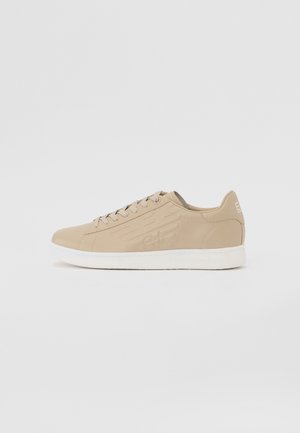 Beżowy niski sneaker na sznurówki, z wytłaczanym wzorem po bokach i białą podeszwą, pokazany z boku na jednolitym tle.