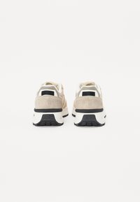 Beige og hvite joggesko med overdel i semsket skinn og mesh, svarte detaljer, polstret krage og teksturert såle. Merket synlig på hælen.