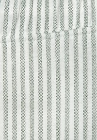 Raidallinen kangas valkoisena ja vihreänä, jossa on ohuita pystysuoria raitoja ja pieniä pistekuvioita. Pehmeä rakenne, kevyt materiaali.