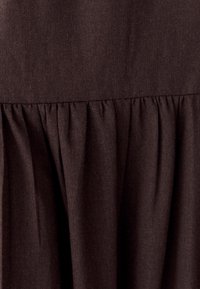 Tmavohnedá tkanina so zloženou textúrou na okraji, so hladkým a rovnomerným povrchom bez viditeľných vzorov alebo akcentov.