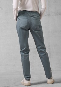 Jasnoniebieskie, zwężające się spodnie z tylnymi kieszeniami, wykonane z gładkiego materiału. Model nosi beżowe sneakersy z delikatnym logo.