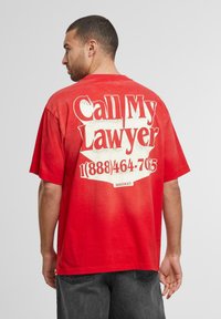 Rød bomulds T-shirt med stort hvidt grafisk tekst på ryggen, der står "Ring til min advokat" med kontakt nummer. Klassisk pasform, korte ærmer.
