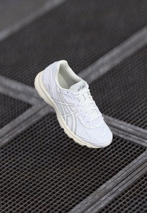 Chaussure de course blanche Asics avec lacets sur une surface en grille métallique sombre vue de dessus.