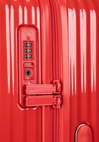 Maleta dura roja con textura acanalada vertical, cremalleras dobles, candado combinatorio y características de seguridad aprobadas por la TSA.