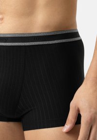 Cofanetto di boxer neri con motivo a righe, dotati di un elastico grigio in vita con il nome del marchio. Il materiale sembra morbido ed elastico.