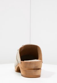 Beige Wildlederschuh mit Holzabsatz, mit glatter Textur und abgerundetem Hinterteil. Die natürliche Holzmaserung ist an der Seite des Absatzes sichtbar.