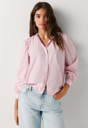Jasnoróżowa koszula na guziki w paski z długimi bufkami, kołnierzykiem i luźnym krojem, zestawiona z jasnoniebieskimi, wysokim stanem jeansami.