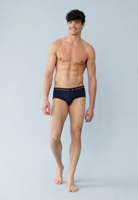 Donkerblauwe katoenen slipjes met een contrasterende tailleband waarop de merknaam in het wit is afgedrukt. De stof lijkt soepel en biedt een nauwsluitende pasvorm.