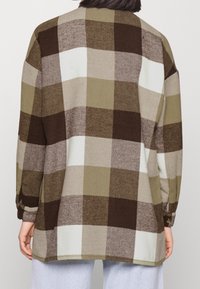 Ruskea, oliivinvihreä ja kermahuuhtoutunut tarkastettu flanelli-paitapusero rentoa istuvuutta, pitkät hihat ja napitetut hihansuut. Pehmeä rakenne hieman löysällä muotoilulla.