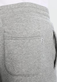 Pantalon de survêtement en coton gris avec une grande poche arrière plate et une petite étiquette de marque sur la poche, avec une texture douce et une ceinture élastique.