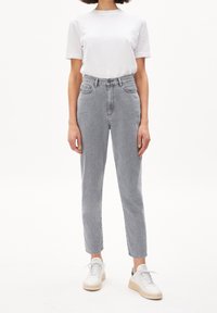 Vaaleanharmaat korkeavyötäröiset farkut, joissa suora leikkaus, viisi taskua ja hienovarainen haalistuma, yhdistetty yksiväriseen valkoiseen lyhythihaiseen t-paitaan ja tennareihin.