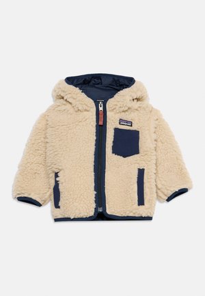 Giacca per bambini in pile color crema con cappuccio, bordino blu navy, cerniera frontale e tasche blu navy davanti e sul petto.