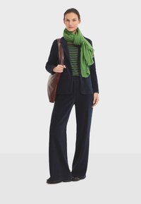 Marinblå kordfloret blazer och vida byxor i kombination med en grön scarf och randig topp. En brun läderaxelväska fulländar looken.