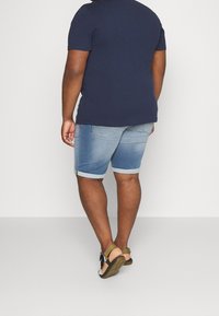 Tmavě modré tričko s krátkým rukávem v kombinaci s světle modrými denimovými šortkami, které mají ohrnuté manžety a volný střih. Outfit doplňují béžové sandály.