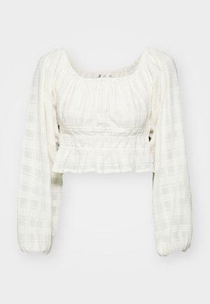 Bluză albă scurtă, cu un model texturat în grilaj, mâneci lungi tip balon, decolteu pătrat și detalii smock la talie.