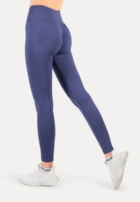 Leggings de talle alto en azul marino con una tela suave y elástica. Presentan un diseño contorneado y costuras laterales. Combinadas con zapatillas deportivas blancas.