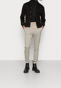 Black denim jacket, fitted black turtleneck, beige plaid trousers, and black chelsea boots with a side pull tab.