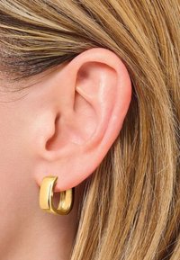 Goldene Creolen, die an einem Ohr präsentiert werden, mit einer glatten, glänzenden Oberfläche und einem massiven, leicht gebogenen Design.