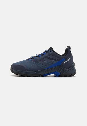 Męskie buty outdoorowe z ciemnoniebieską cholewką z siateczki, trwałą czarną gumową podeszwą oraz niebieskimi akcentami dla lepszej widoczności i przyczepności.