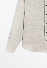 Helle beige Langarmbluse aus strukturiertem Stoff, mit einer knopfbaren Vorderseite in dunkler Farbe und einem geschwungenen Saum.