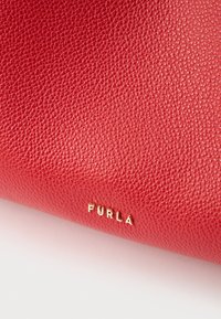 Rød tekstureret læderpung med en kornet finish. Har guldpræget "Furla"-logo. Kompakt form, der forstærker det overordnede design.