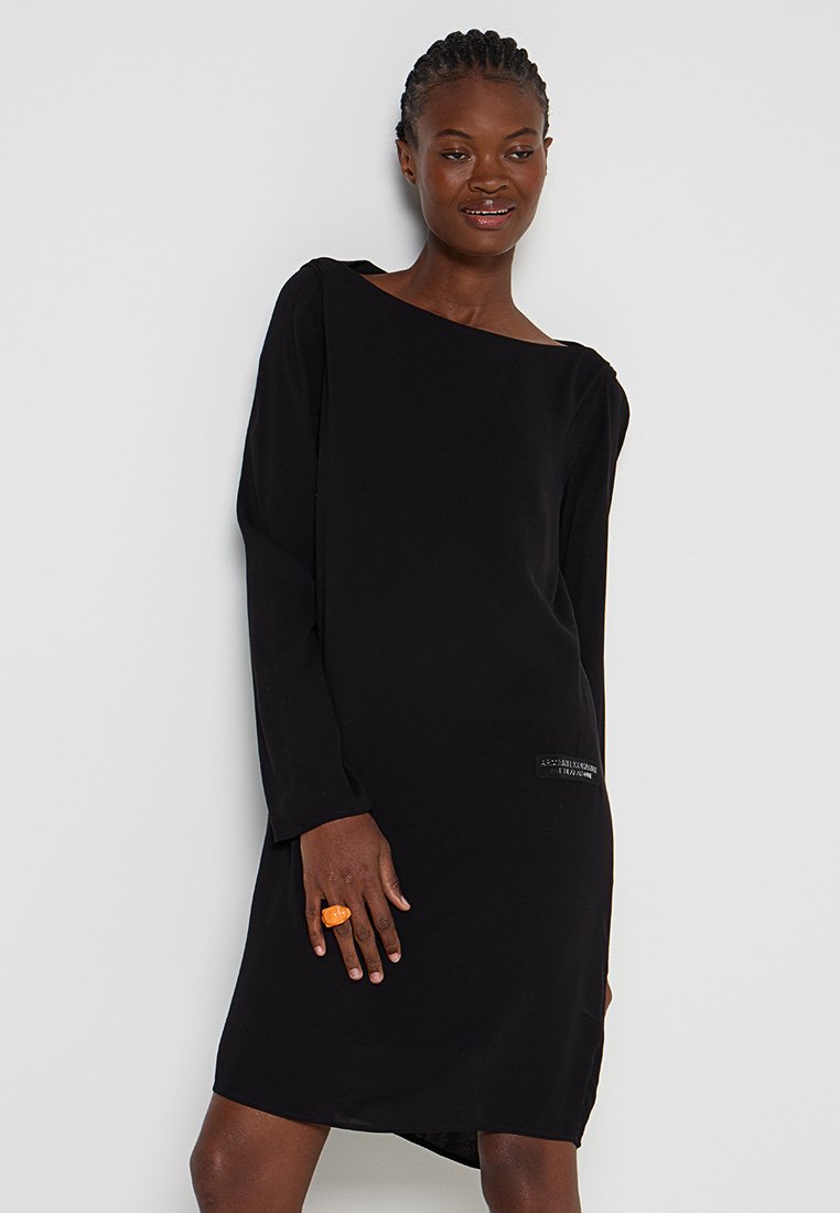 Abito nero a maniche lunghe con design sciancrato e spalle scoperte. Realizzato in tessuto liscio, presenta una patch logo sul lato e un orlo leggermente curvato.