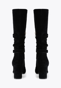 Bottes noires en suede montantes avec un design ample, des talons carrés et des fermetures éclair à l'arrière. Présente un accent de sangle au niveau de la cheville.