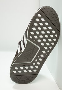 Brown rubber sneaker sole with white hexagonal and circular tread patterns, featuring textured accents and a label with brand name.