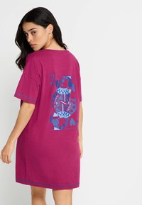 Magenta krátky rukáv T-košeľové šaty s modrou grafickou potlačou na chrbte, ktorá zobrazuje srdcia a abstraktné prvky, s rovným strihom a okrúhlym výstrihom.