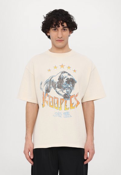 Tricou oversized de culoare crem, cu un grafic al unei pantere negre cu accente albastre și portocalii, înconjurată de cinci stele galbene.