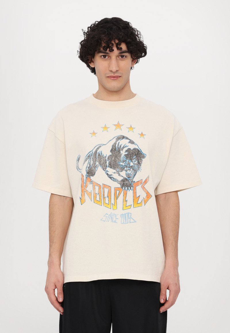Kremfarget oversized t-skjorte med et grafisk motiv av en svart panter med blå og oransje detaljer, omgitt av fem gule stjerner.