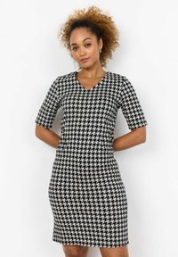 Musta-valkoinen houndstooth-neulemekko, jossa on V-pääntie, lyhyet hihat, istuva malli ja teksturoitu kangas.