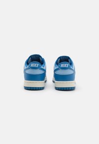 Blå lædersneakers med hvide detaljer, rund tå, polstret krave og struktureret gummisål. "NIKE" logo trykt på hælen.