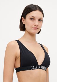 Fekete, háromszög alakú bralette sima anyagból, széles logós pánttal az alján és minimális varrási részletekkel.