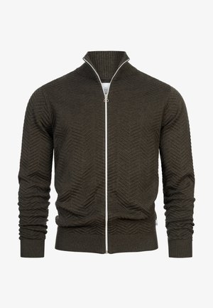 Olivgrön zip-up cardigan med ett texturerat chevronmönster, ribbad krage och mudd. Har en kontrasterande vit dragkedja och fåll.