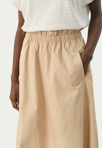 Beige, knee-length skirt with an elastic waistband and side pockets, made from a lightweight fabric with a smooth texture.