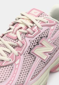 Roosa ja valge New Balance'i tennisekets, kus on võrkkangas, valged lipsud ja suur "N" logo küljel, näidatud lähivõtetes.