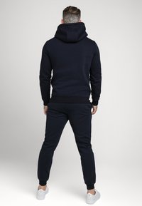 Completo felpa e pantaloni jogger di colore blu navy realizzato in tessuto morbido. Include un cappuccio, polsini e vita a coste. Design semplice senza motivi o decorazioni.