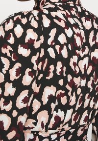 Svart tyg med ett leopardmönster i blush, vitt och vinrött. Har en hög krage och plisserade detaljer.