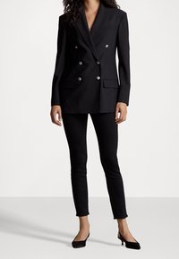 Černý vypasovaný dvoubarevný blazer se stříbrnými knoflíky, zkombinovaný s černými úzkými kalhotami a černými jehlovými lodičkami. Hladká textura látky.