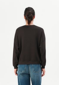 Dark brown sweatshirt with a crew neckline, relaxed fit, and ribbed cuffs. Paired with light-wash, loose-fitting denim jeans.