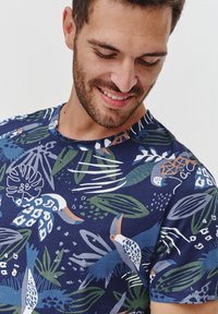 Granatowy T-shirt z krótkim rękawem z tropikalnym nadrukiem zielonych liści oraz motywami ptaków w odcieniach bieli, pomarańczu i niebieskiego. Miękki materiał bawełniany.