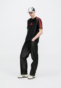 Czarny sportowy t-shirt z czerwonymi paskami i logo, czarne spodnie dżinsowe, białe trampki z czarnymi akcentami oraz szara czapka z czarnymi detalami.