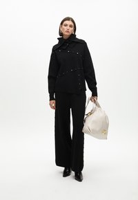 Černý strukturovaný svetr s texturou a límečkem, zlatými akcenty, černé volné kalhoty a měkká béžová kabelka s logem.