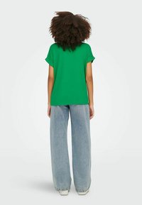 Grønn kortermet t-skjorte med rullecuff, kombinert med høy midje, vide lyseblå jeans og hvite joggesko.
