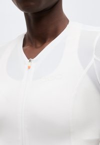 Κοντινό πλάνο προσώπου που φοράει λευκό μπλουζάκι με φερμουάρ και μανίκια από δίχτυ, εμφανίζοντας το πάνω μέρος του στήθους και την περιοχή του λαιμού.