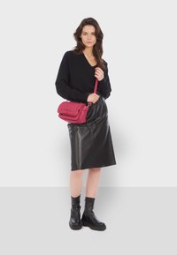 Černý svetr s výstřihem do V, černá kožená sukně na vysokém pasu ve stylu tužky a černé kotníkové boty. Drží růžovou prošívanou crossbody kabelku.