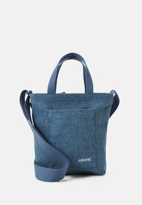 Denim tote bag in dark blue with short handles and a detachable shoulder strap. Features a front pocket and a subtle logo detail.
